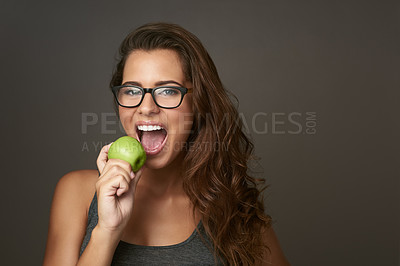 Buy stock photo Studio shot of a beautiful young woman about to bite an apple against a brown background