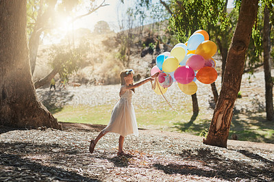 Buy stock photo Shot of a little girl playing with a bunch of balloons outside