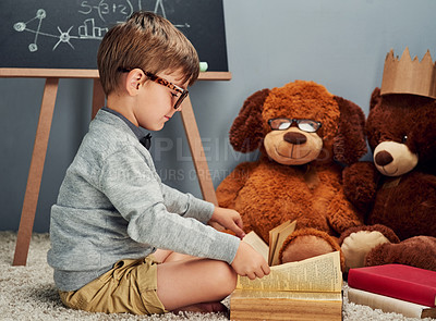 Buy stock photo Studio shot of a smart little boy reading a book to his teddy bears against a gray background