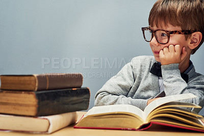 Buy stock photo Studio shot of a smart little boy reading books and looking thoughtful against a gray background