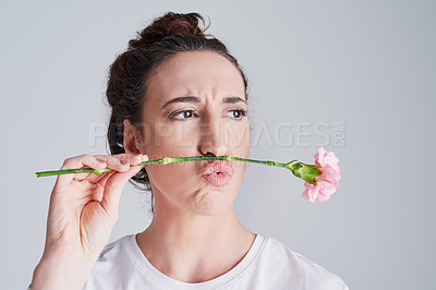 Buy stock photo Studio shot of a beautiful young woman making a face with a flower against a grey background