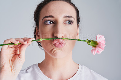 Buy stock photo Studio shot of a beautiful young woman making a face with a pink flower against a grey background
