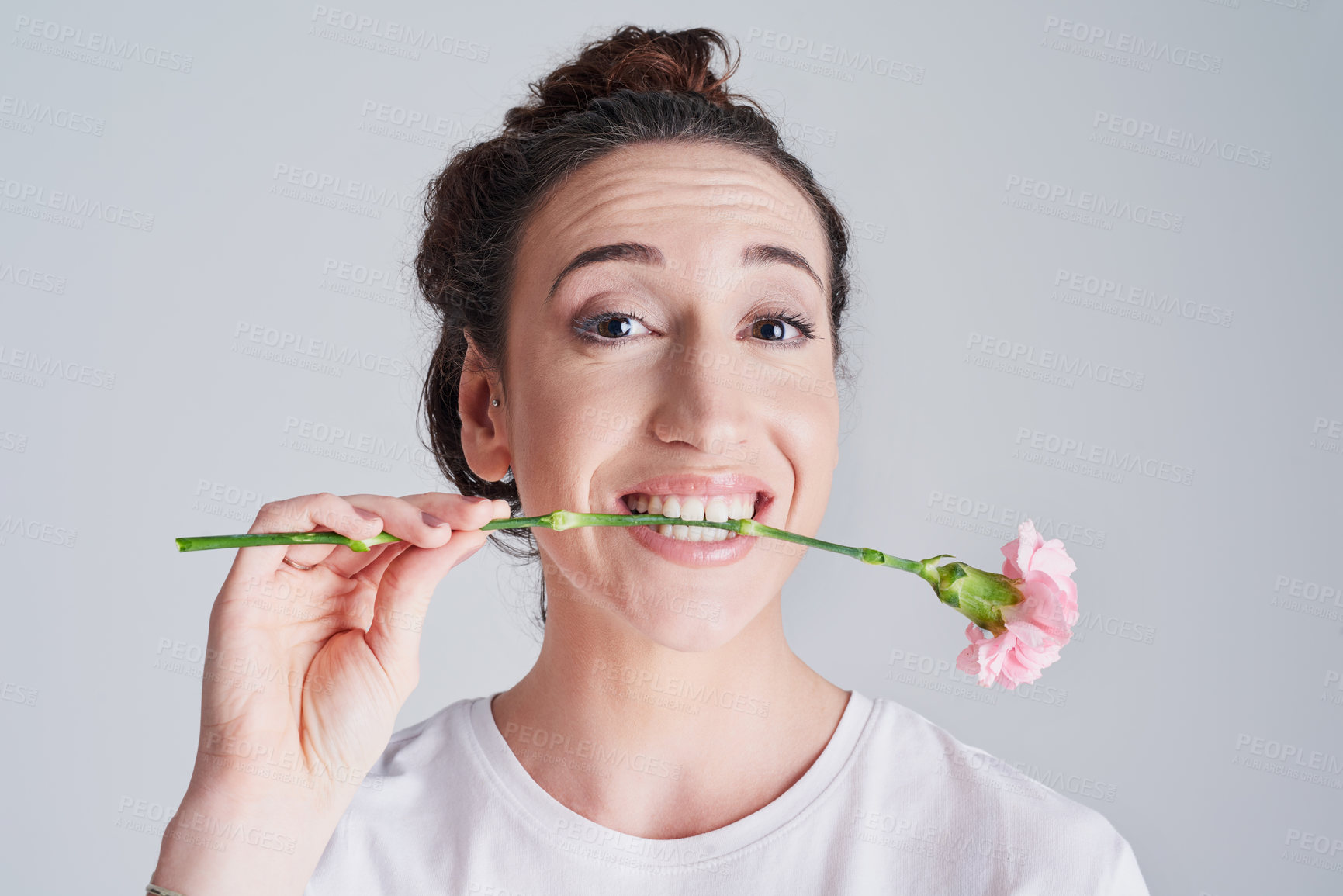 Buy stock photo Studio shot of a beautiful young woman holding a pink flower with her teeth against a grey background