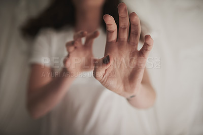 Buy stock photo High angle shot of an unidentifiable young woman holding up her hands in a defensive gesture while lying in bed