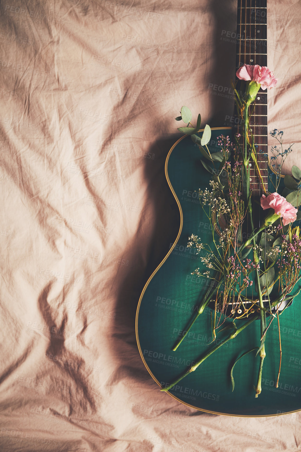 Buy stock photo High angle shot of a green guitar lying on a bed with flowers arranged on it