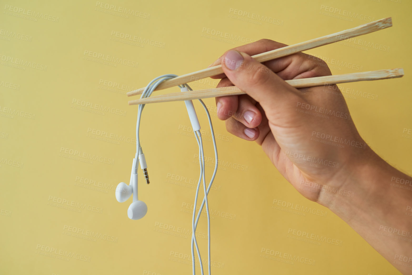 Buy stock photo Cropped studio shot of a man holding earphones wrapped around chopsticks against a yellow background