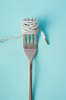 Buy stock photo Studio shot of earphones wrapped around a fork against a blue background