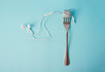 Buy stock photo Studio shot of earphones wrapped around a fork against a blue background