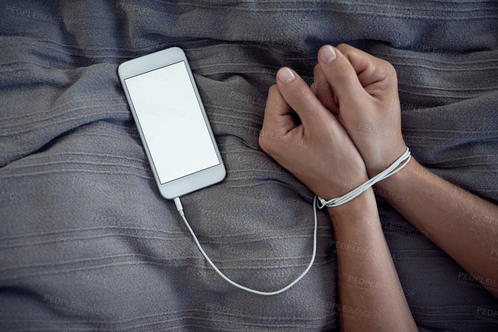 Buy stock photo Cropped shot of a unrecognizable person's hands bound by a cellphone charging cable