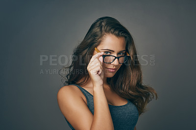 Buy stock photo Studio shot of an attractive young woman peering over her glasses against a grey background