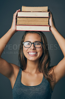 Buy stock photo Studio shot of a young woman holding a pile of books against a grey background