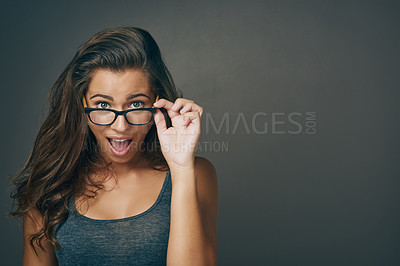 Buy stock photo Studio shot of an attractive young woman peering over her glasses against a grey background