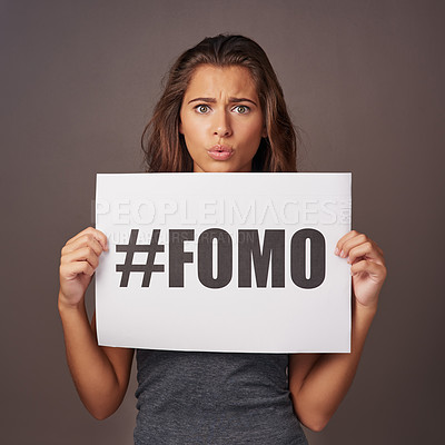 Buy stock photo Studio shot of an attractive young woman holding a sign with #FOMO printed on it against a gray background