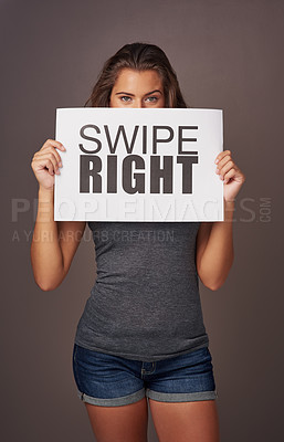 Buy stock photo Studio shot of an attractive young woman holding a sign with swipe right printed on it against a gray background