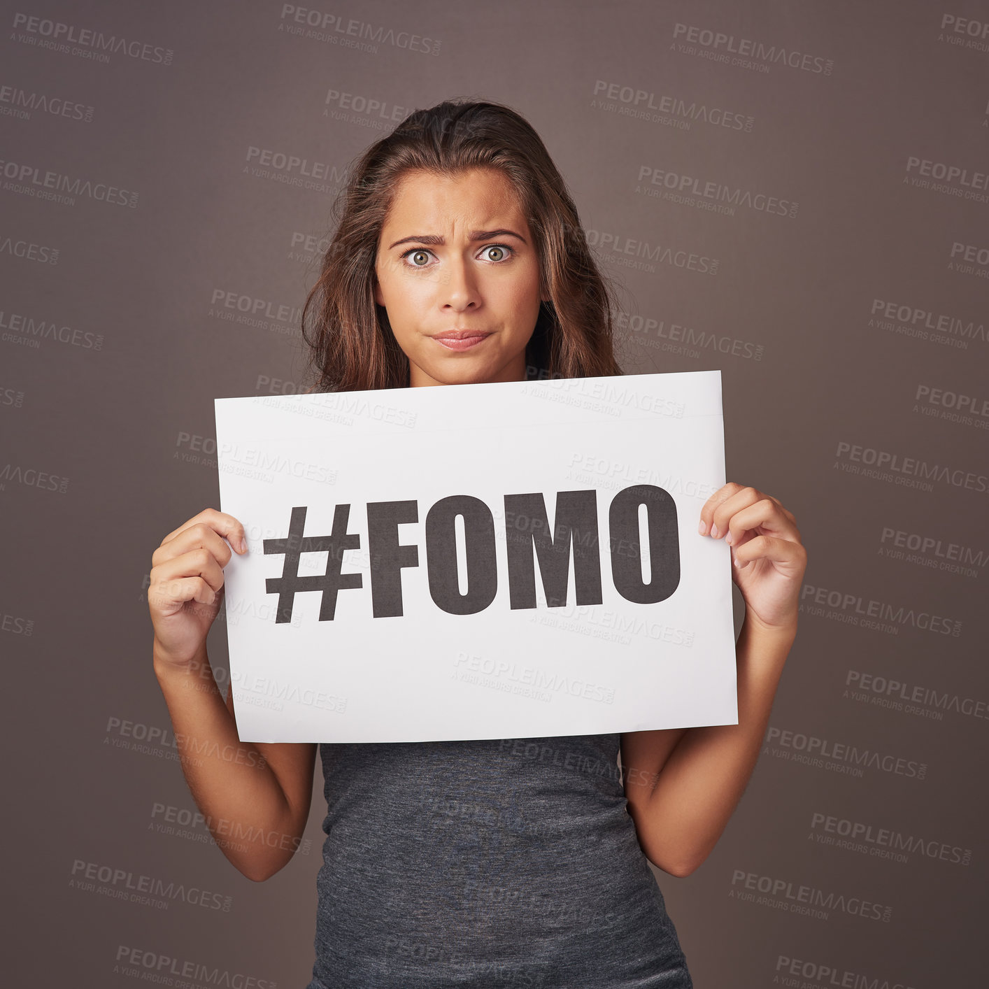Buy stock photo Studio shot of an attractive young woman holding a sign with #FOMO printed on it against a gray background