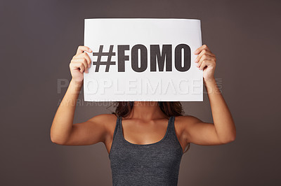 Buy stock photo Studio shot of a young woman holding a sign with #FOMO printed on it against a gray background