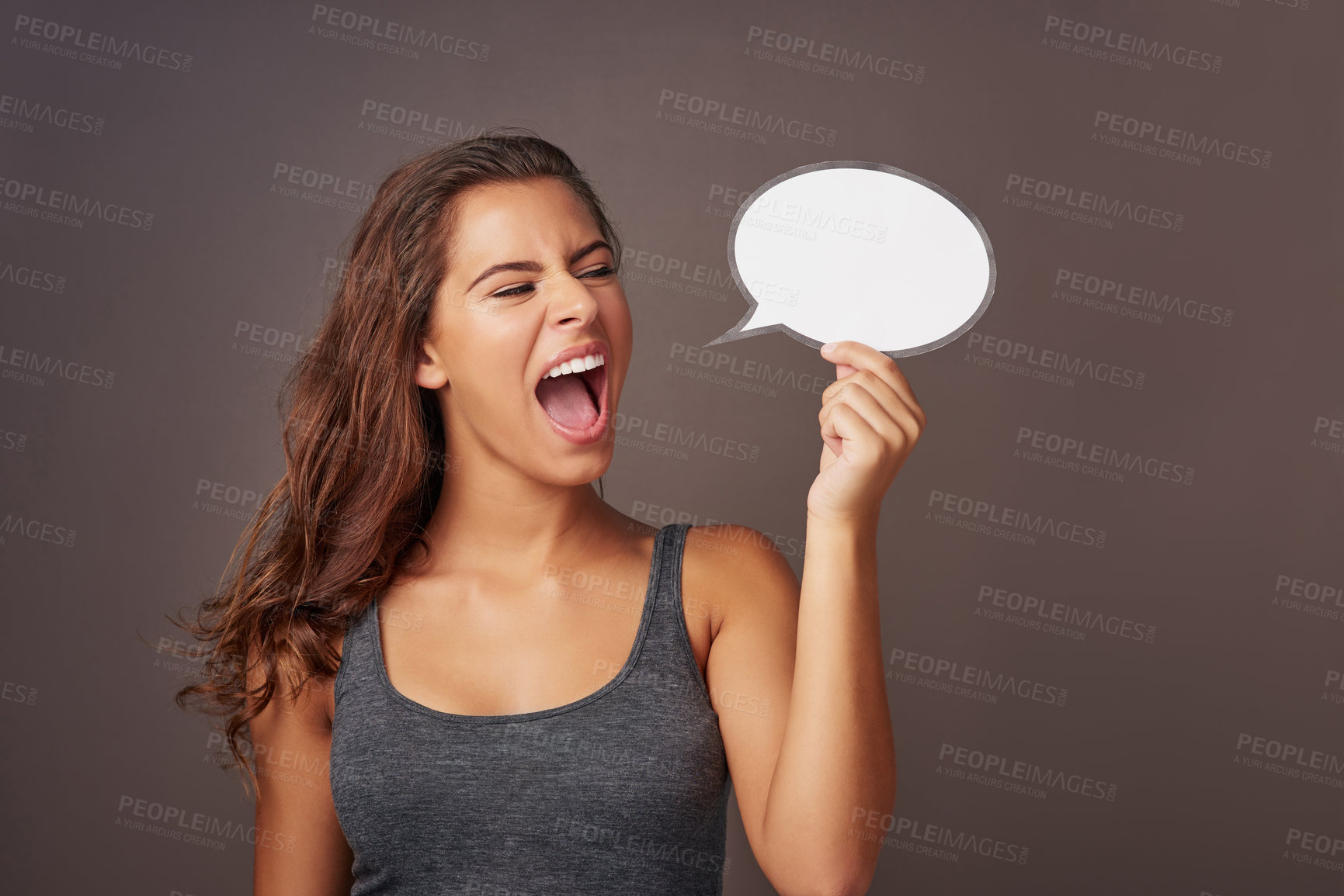 Buy stock photo Studio shot of an attractive young woman holding a blank speech bubble and shouting against a gray background