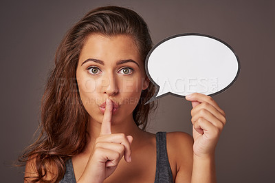 Buy stock photo Studio shot of an attractive young woman holding a blank speech bubble and whispering against a gray background