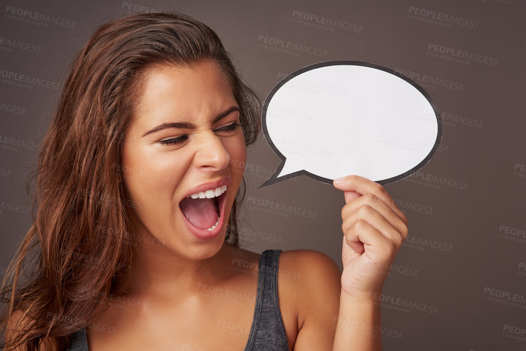 Buy stock photo Studio shot of an attractive young woman holding a blank speech bubble and shouting against a gray background