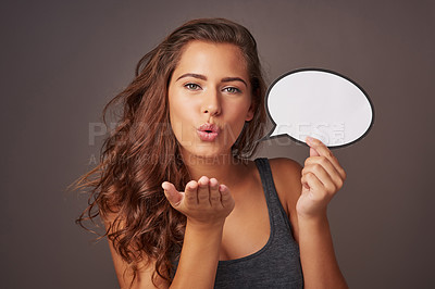 Buy stock photo Studio shot of an attractive young woman holding a blank speech bubble and blowing a kiss against a gray background