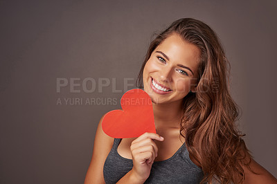 Buy stock photo Studio shot of an attractive young woman holding a blank red heart against a gray background