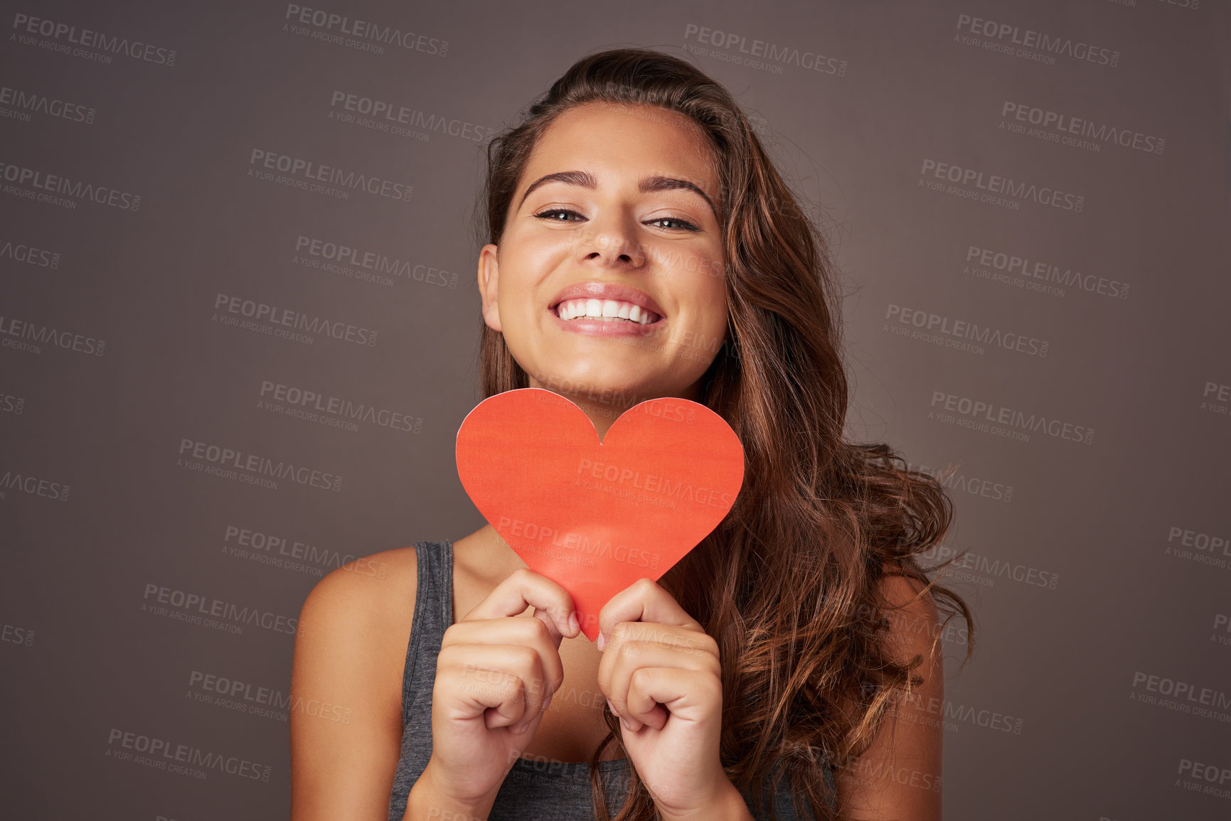 Buy stock photo Studio shot of an attractive young woman holding a blank red heart against a gray background