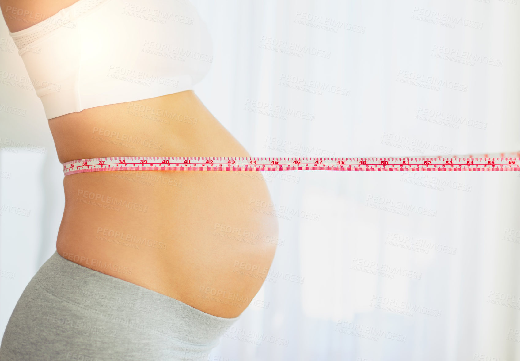 Buy stock photo Cropped shot of a pregnant woman measuring her belly at home