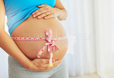 Buy stock photo Cropped shot of a pregnant woman with a tape measure tied around her belly