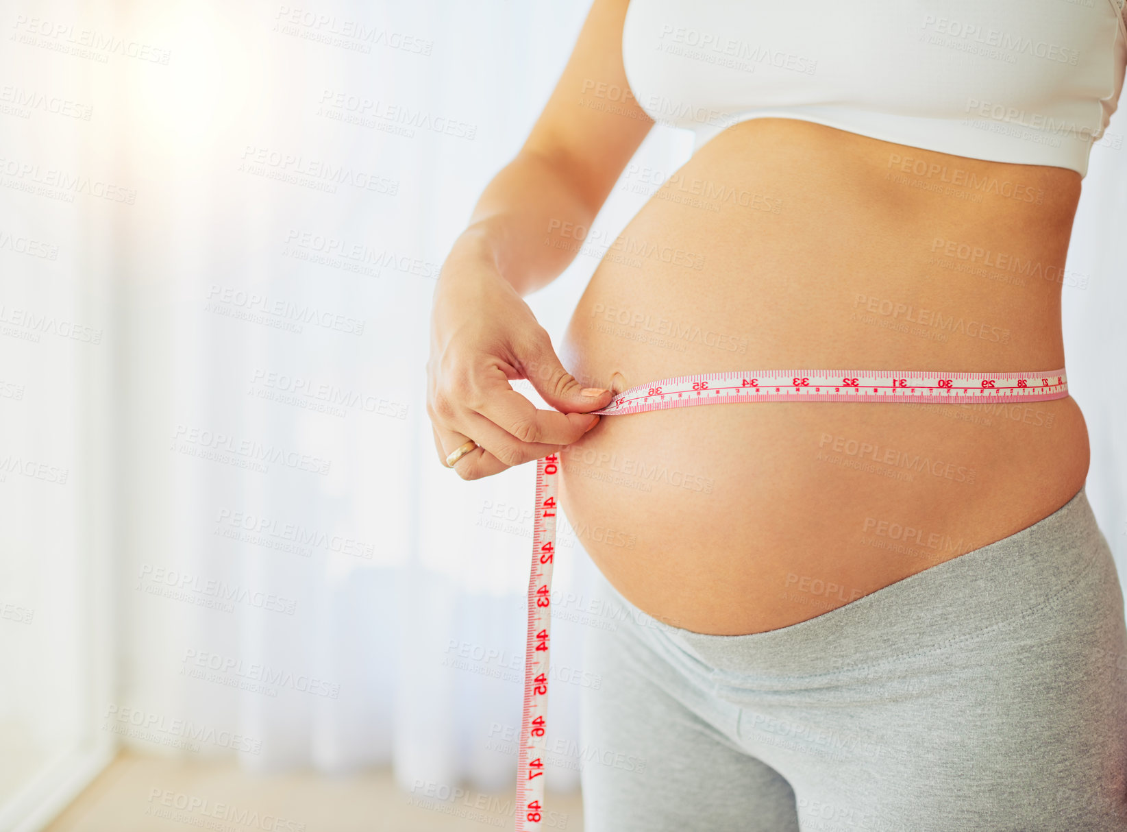 Buy stock photo Cropped shot of a pregnant woman measuring her belly at home
