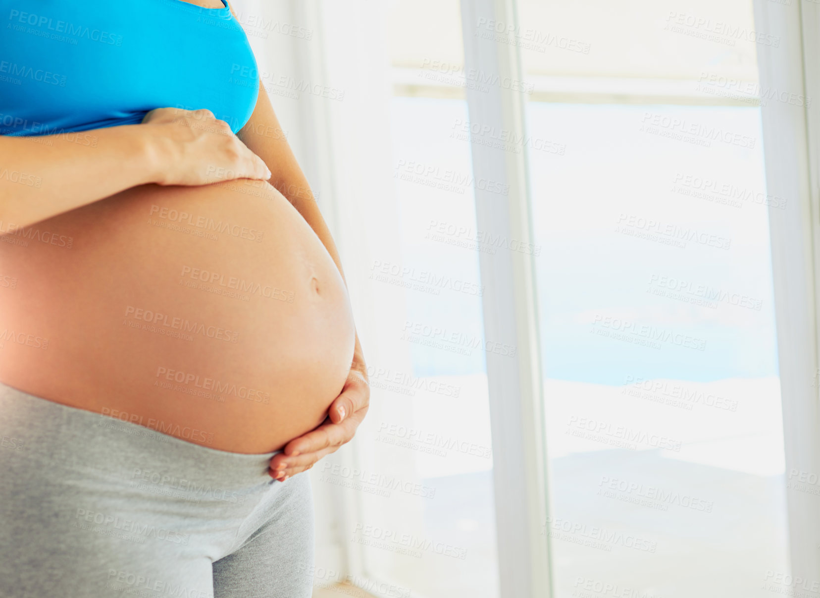 Buy stock photo Cropped shot of a pregnant woman holding her bare belly at home