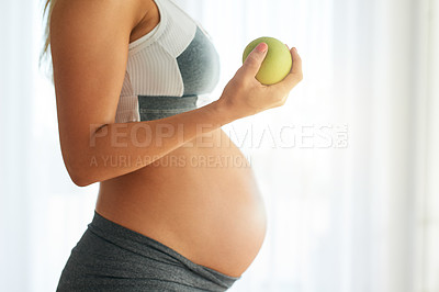 Buy stock photo Cropped shot of a pregnant woman dressed in sportswear and eating an apple at home