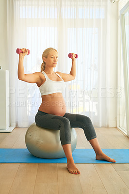 Buy stock photo Shot of a pregnant woman working out with an exercise ball and weights at home