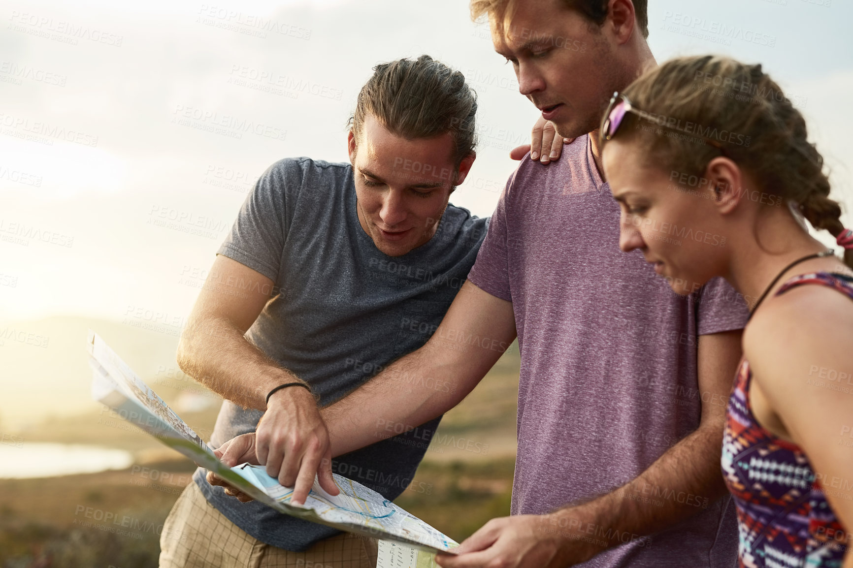 Buy stock photo Shot of three young hikers consulting a map while exploring a new trail