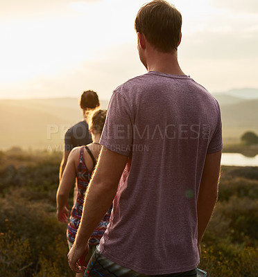 Buy stock photo Friends, people hiking and trekking in countryside with fitness at sunset, nature with travel together and freedom. Exercise, adventure with men and woman walk through meadow or field with back view