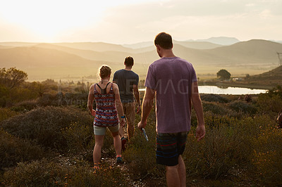 Buy stock photo Friends hiking, walking in countryside at sunset with fitness and bonding in nature with travel and freedom. Exercise, adventure with men and woman walk through meadow or field with back view