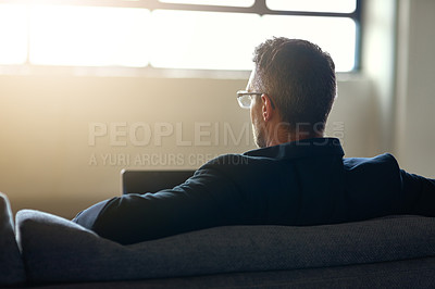Buy stock photo Rearview shot of an unidentifiable businessman using his laptop while sitting on a couch in the office
