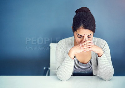 Buy stock photo Shot of an overwhelmed young businesswoman holding her head in her hands while sitting at her desk