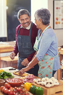 Buy stock photo Shot of a happy mature couple looking at one another while preparing a meal together at home