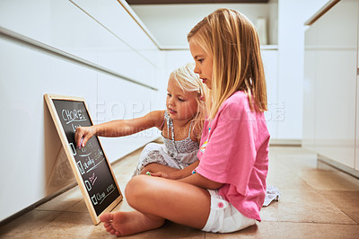 Buy stock photo Shot of two little girls writing a list of chores on a chalkboard at home