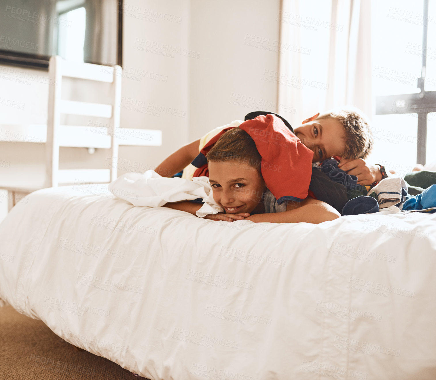 Buy stock photo Portrait of two little brothers lying on a bed under a pile of laundry at home