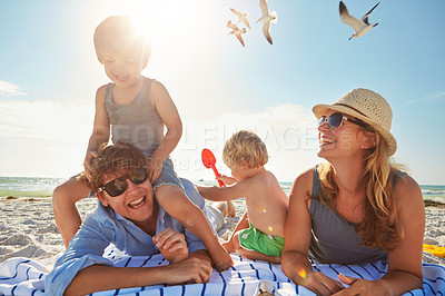 Buy stock photo Picnic, piggyback or children with parents at beach on holiday vacation or happy family weekend together. Father, fun mother or kids siblings at sea for bonding or playing in nature in Spain to relax