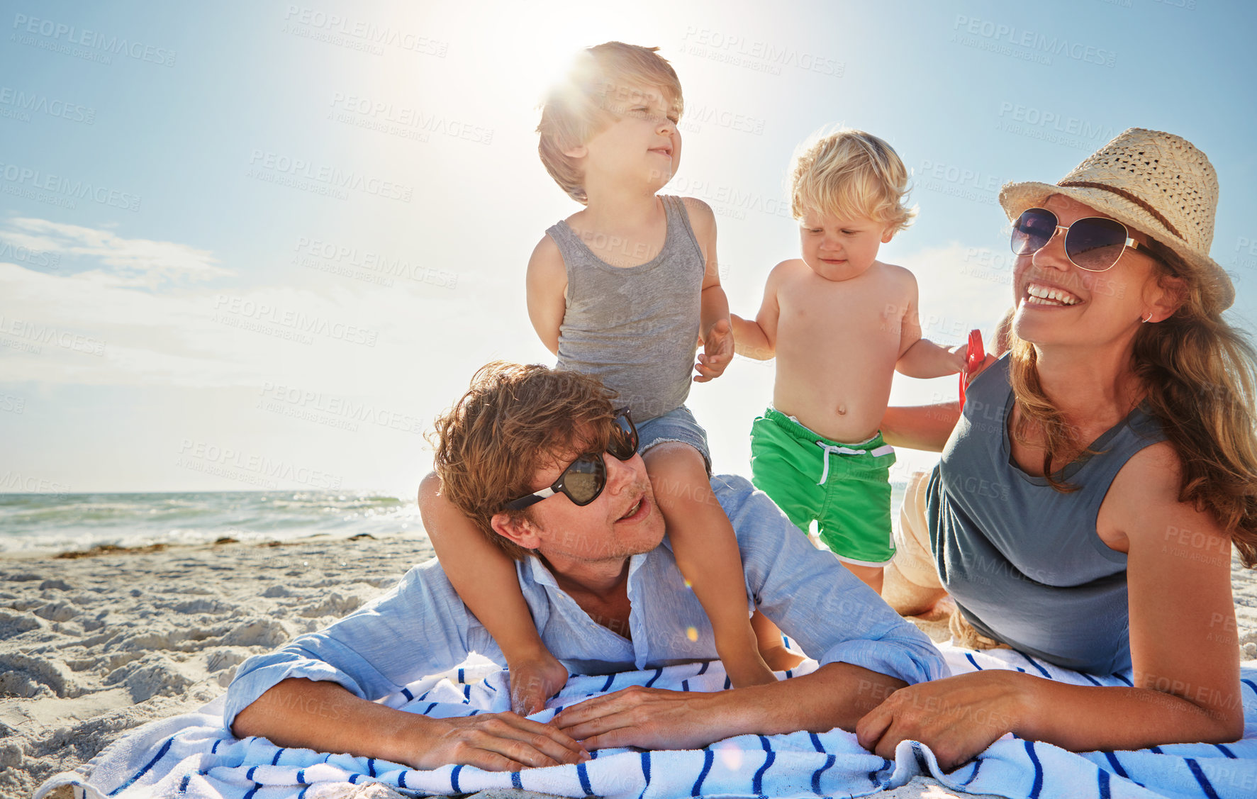 Buy stock photo Picnic, piggyback or children with family at beach on holiday vacation or weekend together with parents. Father, mother or happy kids siblings at sea for bonding or playing by ocean in Spain to relax