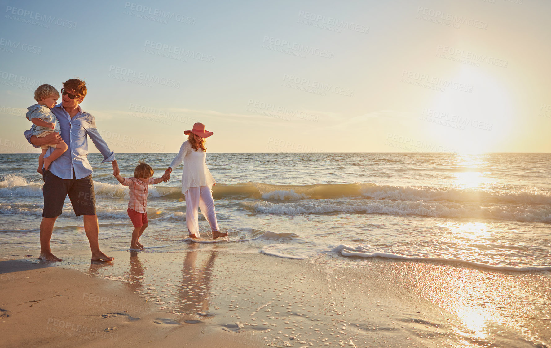 Buy stock photo Family, parents and walking with kids on beach in sunset for outdoor holiday or weekend in nature. Mom, father or children by water holding hands, love or care in sunshine by ocean coast or sea