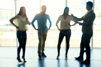 Buy stock photo Defocussed shot of a group of businesspeople brainstorming together in front of a window in the office