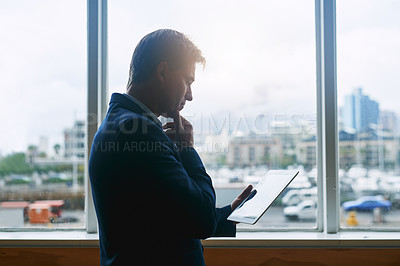 Buy stock photo Shot of a mature businessman working on a digital tablet while standing at a window in an office