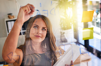 Buy stock photo Shot of an inspired young businesswoman laying out a business plan with adhesive notes against a glass wall