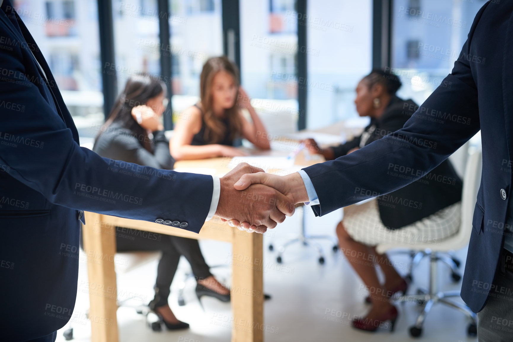 Buy stock photo Cropped shot of two unidentifiable businessmen shaking hands in the boardroom with their colleagues in the background