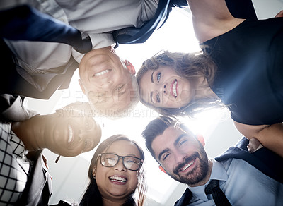 Buy stock photo Low angle portrait of a team of happy colleagues putting their heads together in a huddle in the office