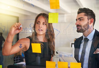 Buy stock photo Shot of a young businesswoman presenting an idea to her colleague using a glass wall and adhesive notes in the office