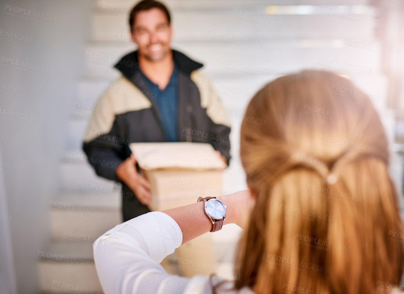 Buy stock photo Shot of a businesswoman checking the time on her watch as the courier arrives with a delivery